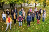 Gruppe von Studierenden steht im Herbstlaub unter Bäumen