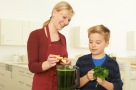 Frau und Kind geben Obst und Gemüse in einen Mixer